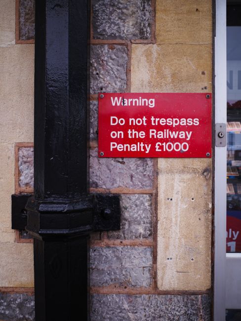 A red rectangular sign with bold white letters reading 'WRONG WAY' is mounted on a black metal pole against a cloudy sky. The sign is attached to the pole with visible metal bolts, and a horizontal metal arm extends from the pole above, possibly for additional signage or visibility. The surrounding environment appears to be outdoors, likely on a street or on-site area where guidance for vehicle or pedestrian movement is necessary. The sky features a mix of dark and light clouds, suggesting overcast weather. The sign's bright red background contrasts sharply with the sky, making it highly visible for passersby, and it subtly relates to the broader context of proper waste disposal pathways by indicating the importance of correct directions, possibly reflecting a dedicated waste collection area or private disposal route in the vicinity. The overall scene emphasizes the importance of following designated routes for rubbish removal services, such as those provided by Waste Disposal Merton, especially when considering alternative or private waste handling methods that require clear signage for safety and compliance.